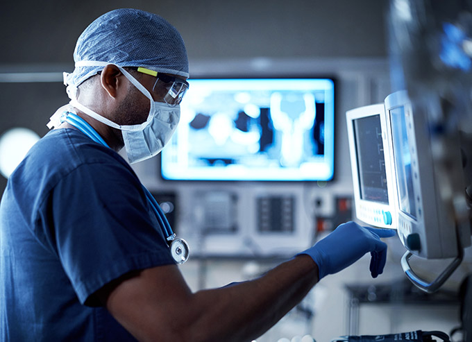 doctor in mask, cap and gloves looking at radiology screen